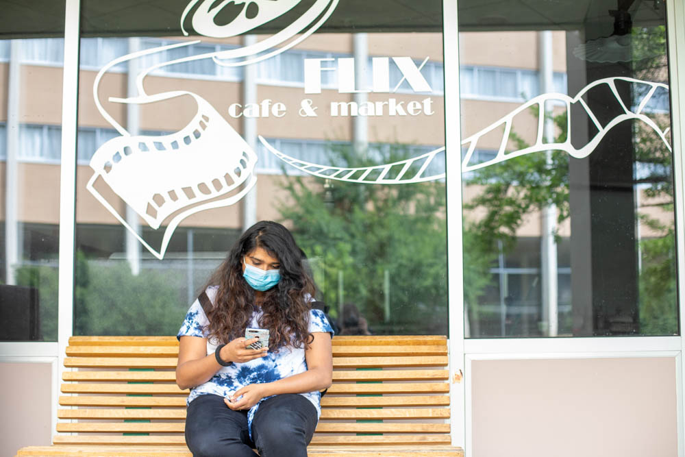 A student sits on a bench outside Flix Cafe and checks their phone.
