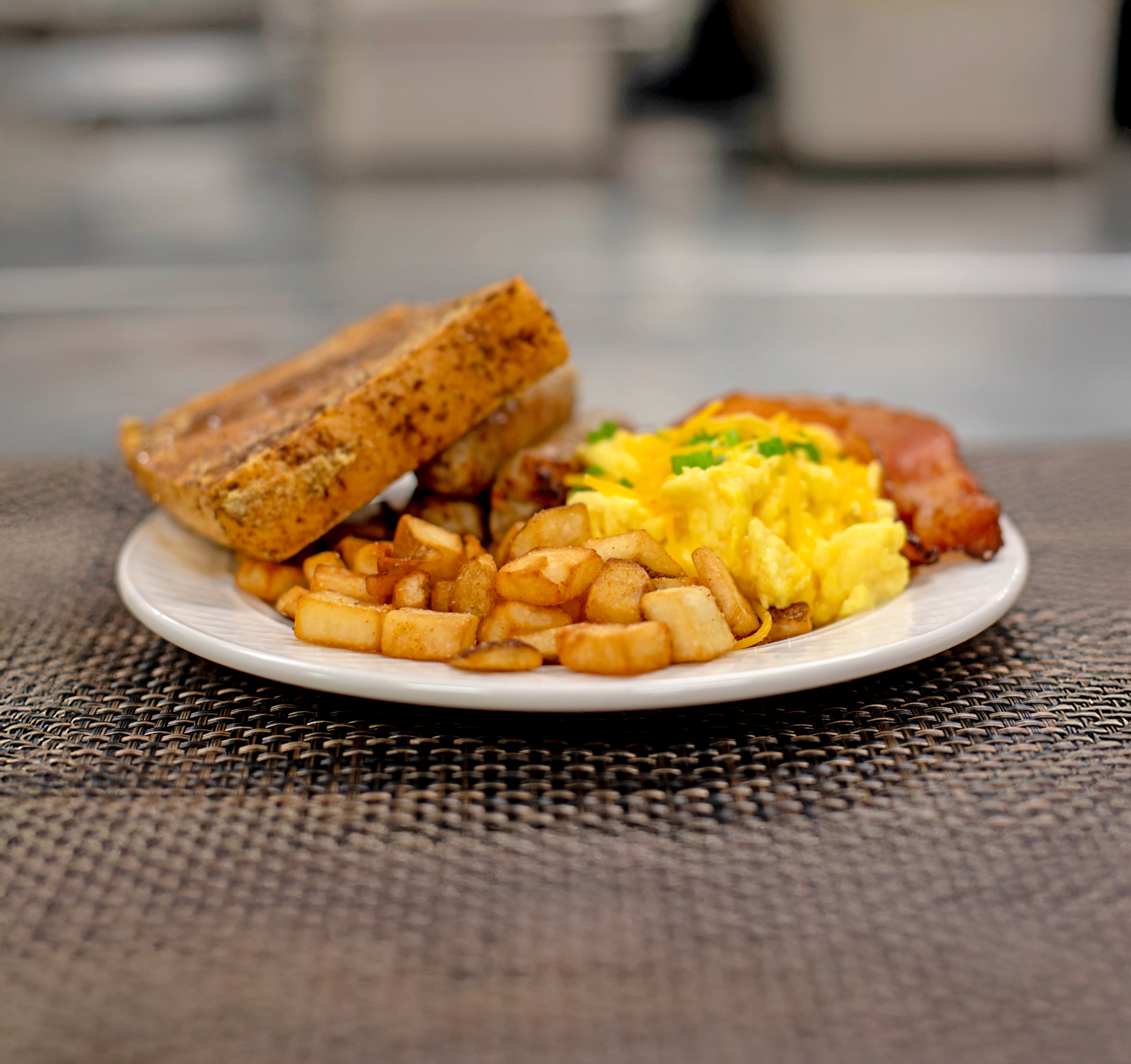 A plate of breakfast food: French toast, scrambled eggs, bacon, and hash browns.