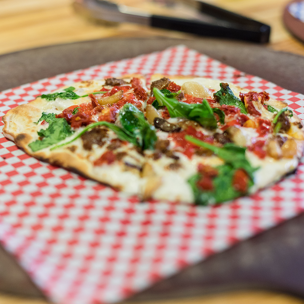 A pizza with spinach and dried tomatoes. 